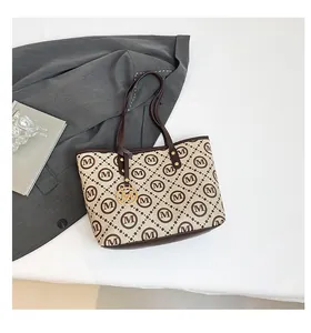 Détail du sac cabas avec motif M répétitif, pendentif doré et poignée marron foncé