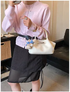 Detail of white lychee leather bucket bag with cute plush bear charm in a chic outfit