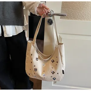 Detailed view of beige canvas hobo bag featuring cute embroidered bear and cat motifs