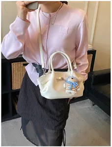 Detail of cream white lychee leather bucket bag featuring a cute knitted bear charm