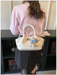 Rear view of a model carrying a white lychee grain bucket bag with a cute bear charm