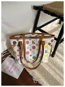 Close-up of white tote bag with colorful monogram print and brown leather trim details