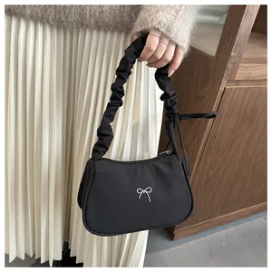 Detalle del bolso de tela negra con asa plisada y adorno de mariposa plateada en metal