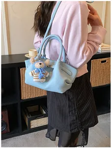 Detail of light blue bucket bag with pebble leather texture and cute teddy bear charm