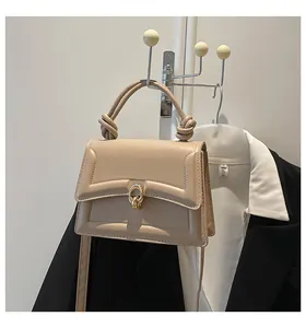 Detail showing beige crossbody bag with knotted handle and golden ring lock against a dark suit