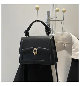 Close-up of black leather handbag with a gold oval clasp and knotted handle detail