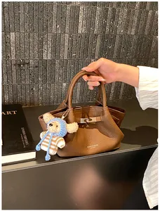 Close-up of brown litchi grain leather bucket bag with cute bear charm and fashion logo