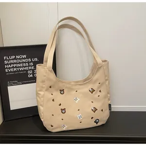 Close-up of embroidered cat patterns on beige canvas tote bag with brand label