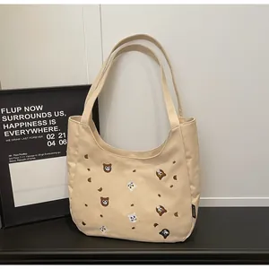 Close-up of cute cartoon bear embroidery and black brand tag on beige canvas tote bag
