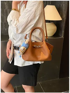 Detail of caramel leather bucket bag with textured grain and blue knit bear charm