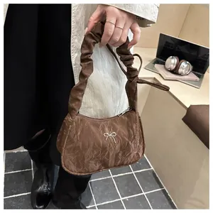 Détail d'un sac à main marron foncé plissé avec nœud métallique argenté et anse froncée
