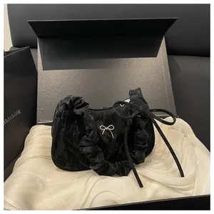 Détail du tissu noir plissé brillant et du petit nœud argenté sur le sac à main chic