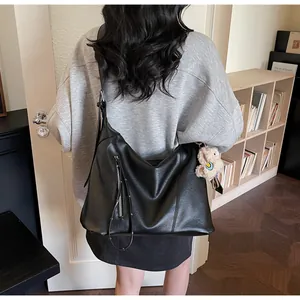 Détail d'un grand cabas noir en cuir avec fermeture éclair et charm d'ours en peluche