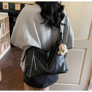 Gros plan d'un sac bandoulière en cuir noir avec zip décoratif et breloque en peluche