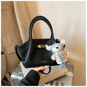 Detail of black lychee grain leather bucket bag with silver lock and plush bear charm