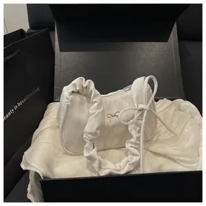 Détail du sac demi-lune plissé blanc avec texture satinée et breloque nœud argenté en coffret