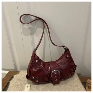 Detail of dark red crescent bag with silver buckles and studs on a textured background