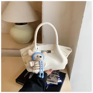 Detail of cream white leather bucket bag with silver lock and a cute plush bear charm