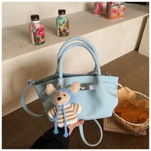 Detail of light blue bucket bag with leather texture and cute plush bear charm decoration
