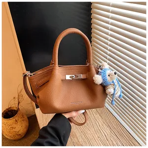 Close-up of brown litchi leather bucket bag featuring a cute teddy bear charm
