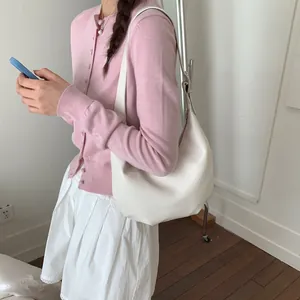 Close-up of a minimalist cream-colored hobo bag worn by a model in a pink cardigan