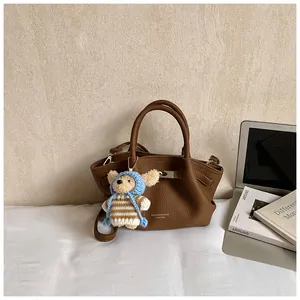 Detail of a brown leather bucket bag with a metal buckle and a cute teddy bear charm