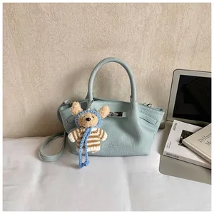 Detail of light blue leather bucket bag with metal buckle and cute bear bag charm