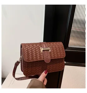 Detail shot of brown woven leather texture and gold metal buckle on a small square bag