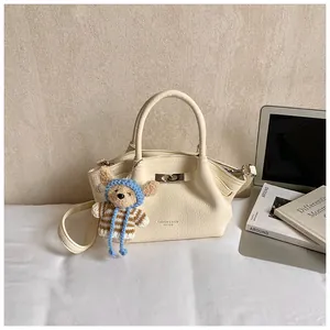 Detail of cream bucket bag with lychee leather texture, twist lock and cute bear charm
