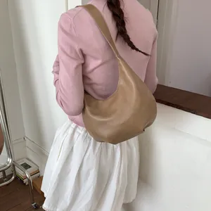 Brown leather crescent hobo bag with wide shoulder strap worn by a model in casual attire
