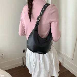 Side view of a black crescent shoulder bag with adjustable silver eyelets strap worn by model