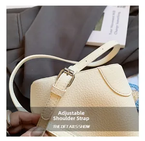 Detail view of adjustable strap with metallic buckle on beige leather bucket bag