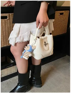 Detail of white lychee leather bucket bag with silver knob and cute teddy bear charm