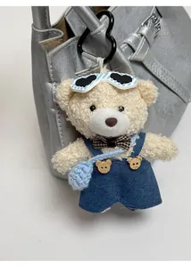 Detail of a fluffy teddy bear charm with sunglasses and blue denim overalls on a handbag