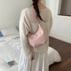 Model wearing a light pink hobo bag on shoulder against a minimalist interior background