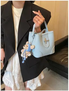 Detail of light blue bucket bag in lychee leather featuring a teddy bear charm and metal clasp