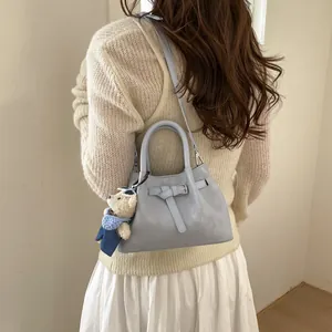 Detailed side view of light blue leather bucket bag with cute teddy bear charm on model