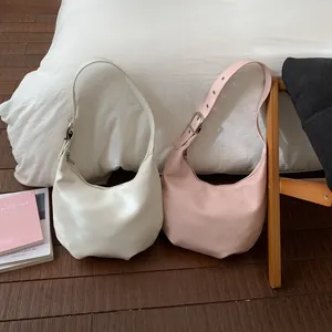 Detail of Korean crescent shoulder bags with adjustable metal buckle straps on white bedding
