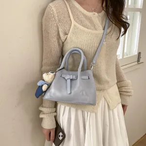 Detail view of light blue bucket bag with belt decor, long strap and bear charm
