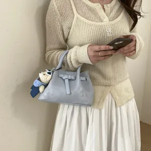 Detail of light blue bucket bag with decorative strap, silver buckle and cute teddy bear charm