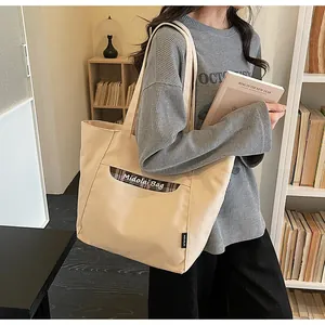 Dettaglio della borsa tote in tela beige con tasca a quadri marroni e tracolla