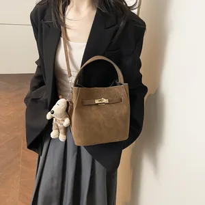 Braune Wildleder-Eimertasche mit Drehverschluss und Plüschtier-Anhänger am Model