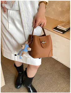 Brown lychee-textured bucket bag with a cute blue knitted bear charm and metal buckle
