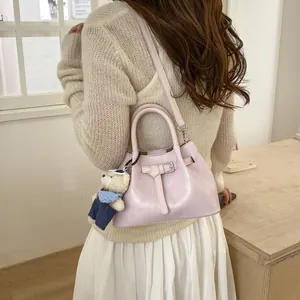 Detail view of pink bucket bag with leather strap, metal buckle and plush bear charm