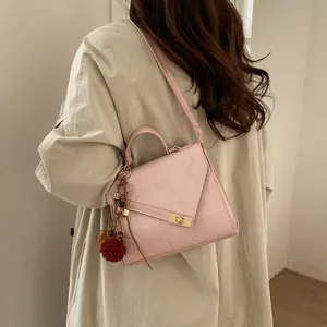Detail of light pink crossbody bag with textured leather, gold lock and plush pendant