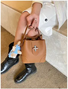 Detail of brown leather bucket bag with silver clasp and a cute teddy bear charm