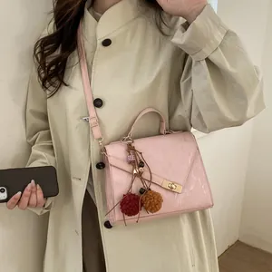 Detail of pink crossbody bag with bohemian charm and gold turn-lock on beige trench coat