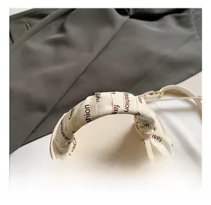 Detail of cream round bucket bag handle wrapped with a printed silk scarf and gold hardware
