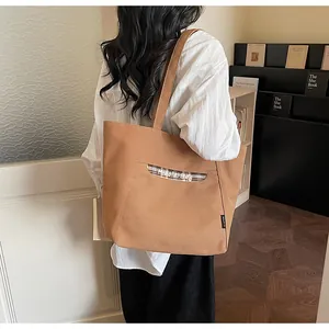 Dettaglio della borsa tote in tela marrone con tasca frontale scozzese e etichetta logo