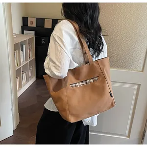 Dettaglio della borsa tote in tela marrone con cinturino scozzese e logo del marchio